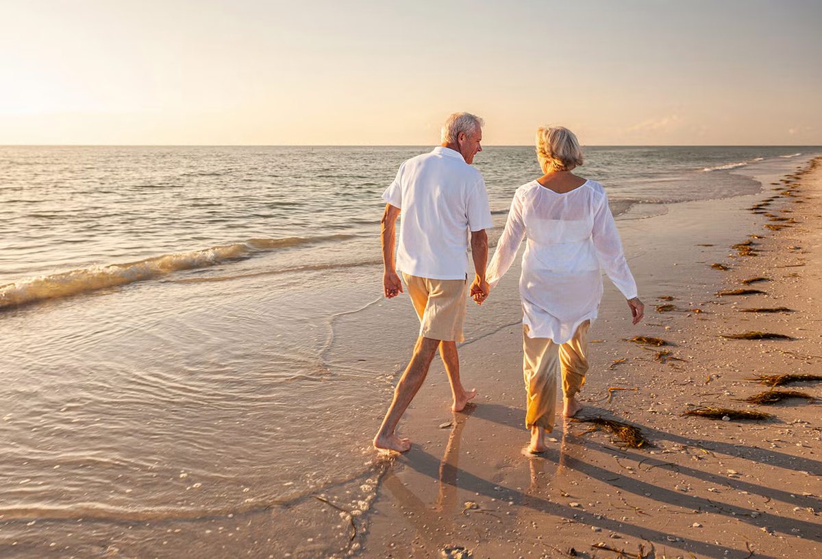 A retired couple walking hand in hand along a Florida beach at sunset